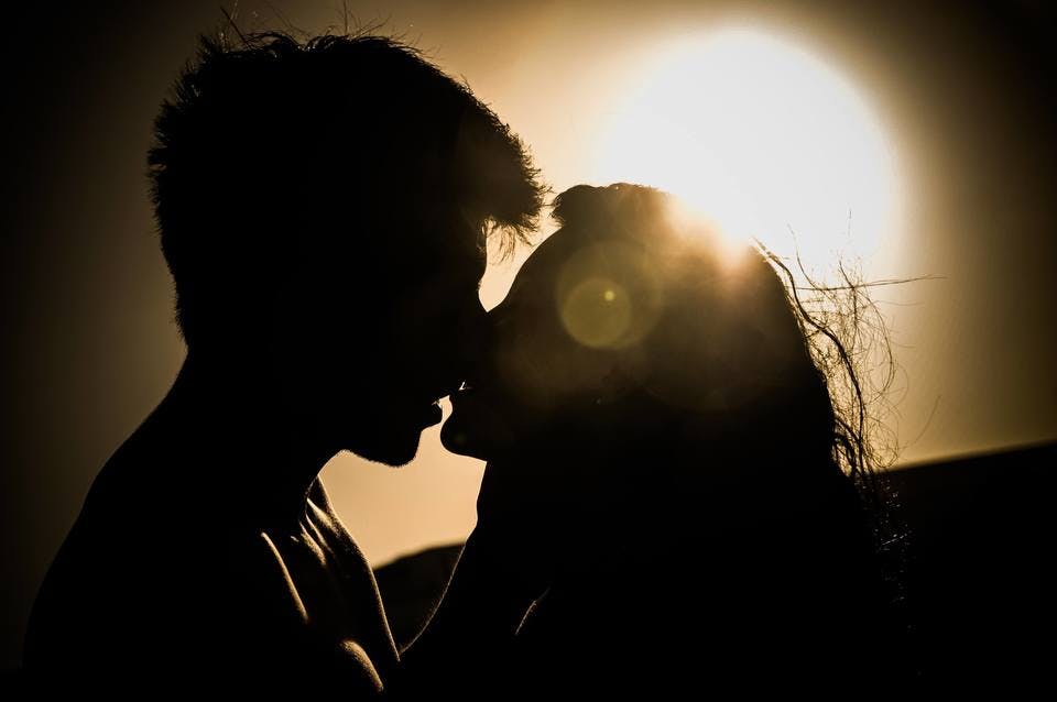既婚者の男性と夕日をバックにキスをする
