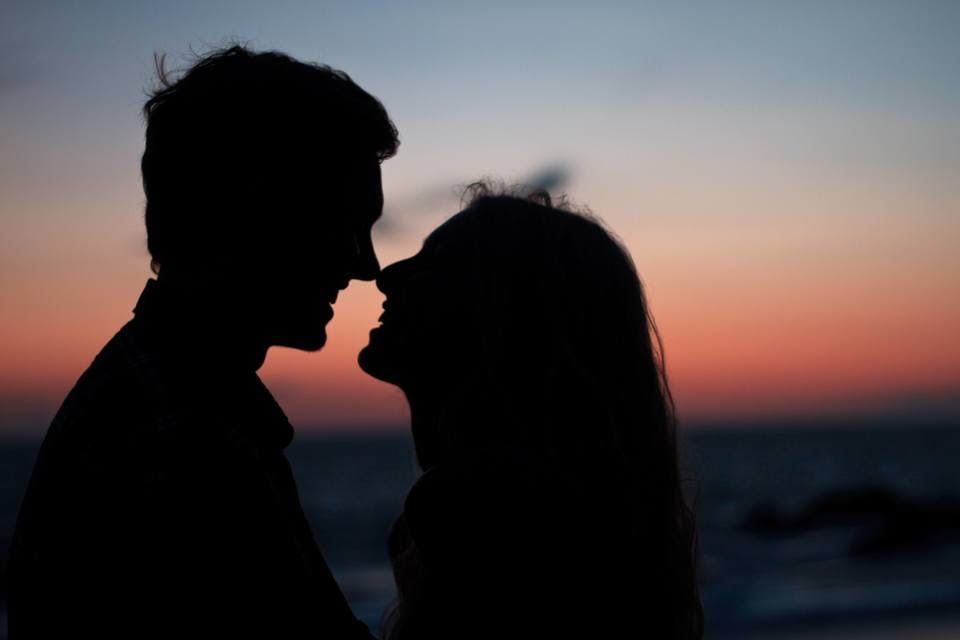 夕陽をバックに見つめ合うキスの種類をしているカップル